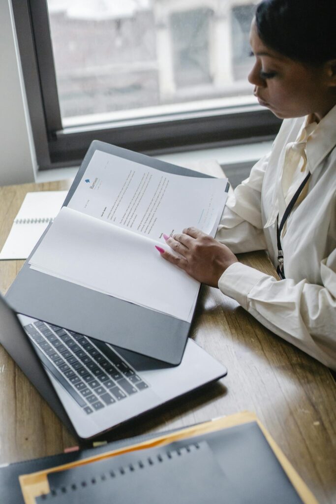 African American woman analyzing financial documents on a laptop, showcasing professional focus.